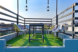 Een terras op het dak met een metalen tafel en stoelen, omringd door een metalen reling en beplanting.