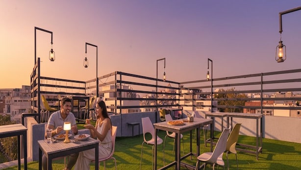 Un espace de restauration aménagé sur le toit, avec des tables et des chaises, une vue sur le paysage urbain et des lanternes décoratives.