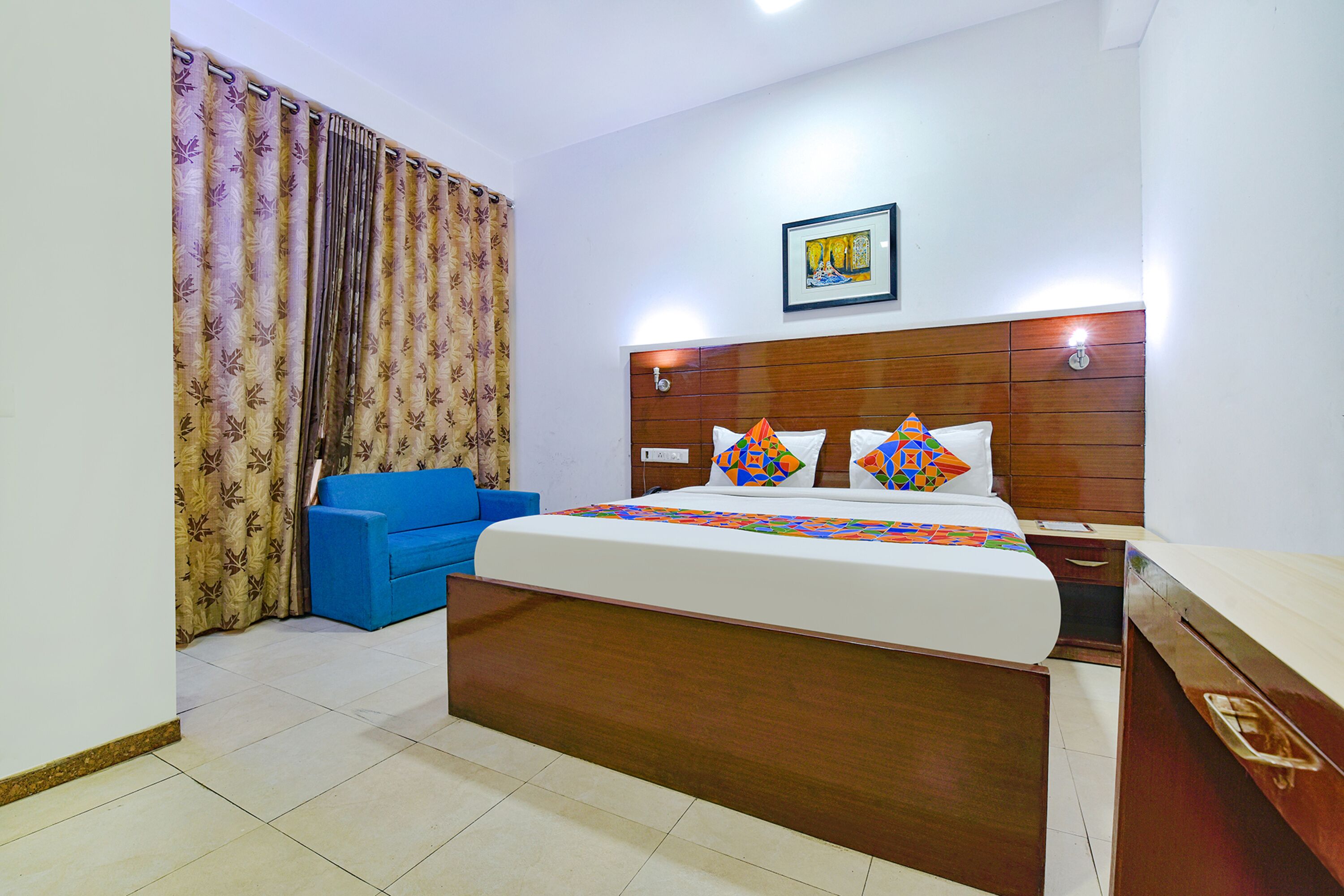 A hotel room with a large bed, a blue sofa, a wooden headboard, and a framed picture on the wall.