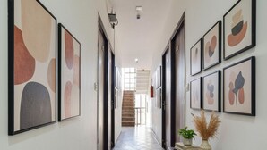 Un couloir orné de tableaux abstraits encadrés, une console en bois sur laquelle est posée une plante, et un escalier en arrière-plan.