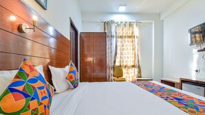 Une chambre d’hôtel avec une tête de lit en bois, un lit avec une literie blanche, des oreillers colorés, un bureau et une chaise.