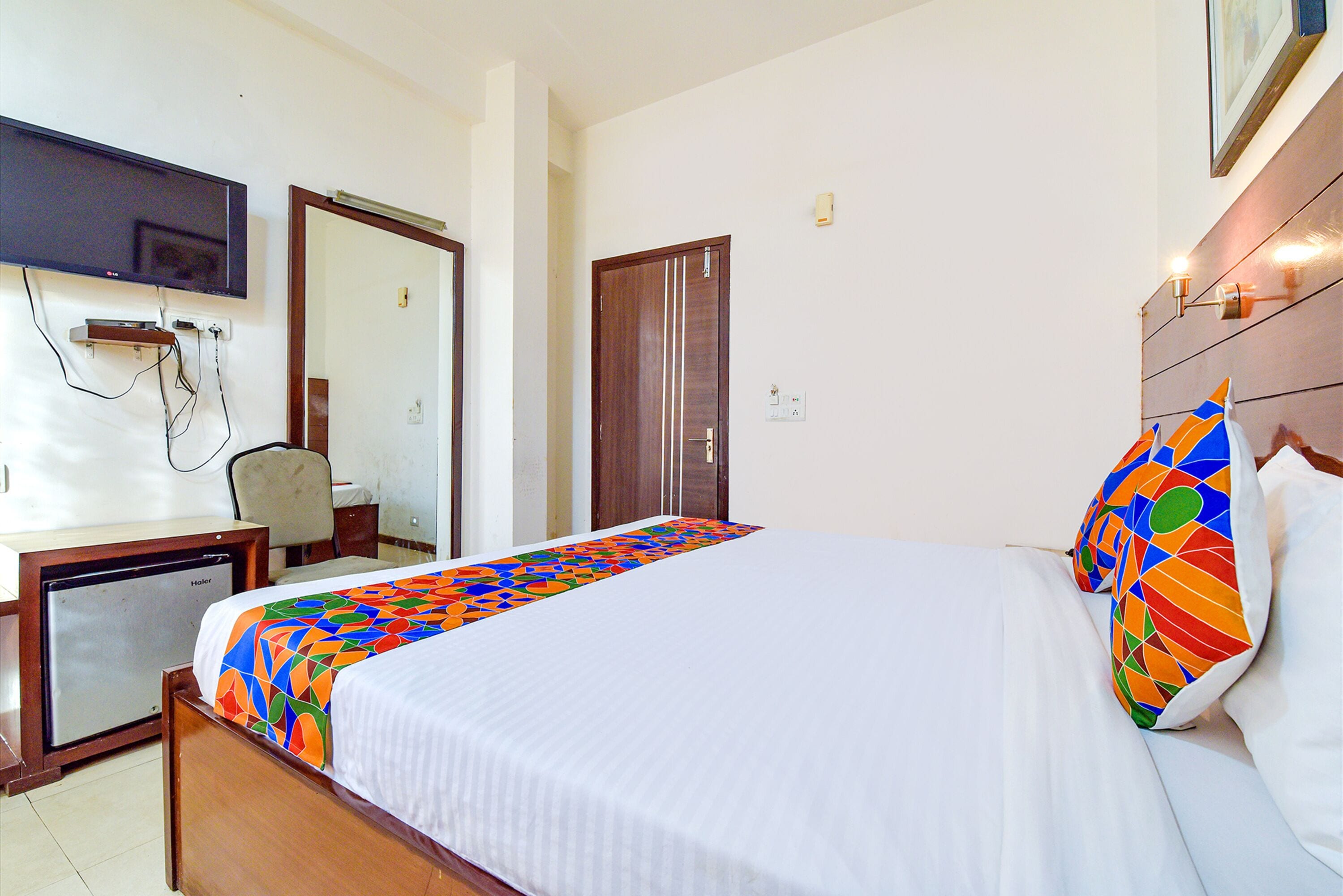 Una habitación de hotel con una cama, un escritorio y televisión, y una puerta.