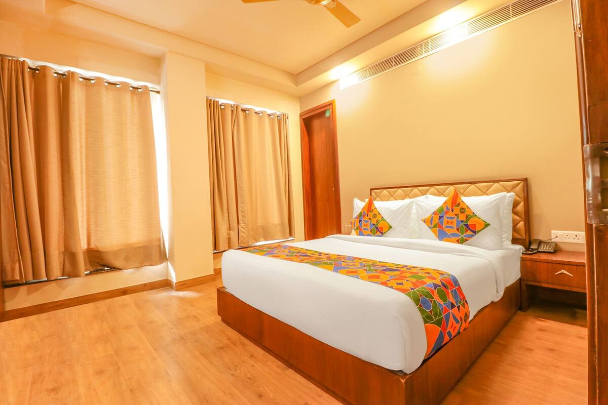 A hotel room with a large bed, a wooden headboard, a bedside table with a phone, and a window with curtains.