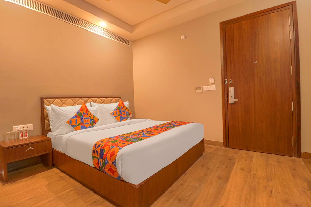 A neatly made bed with a patterned bedspread, a wooden nightstand with a drawer, and a wooden door in a hotel room.