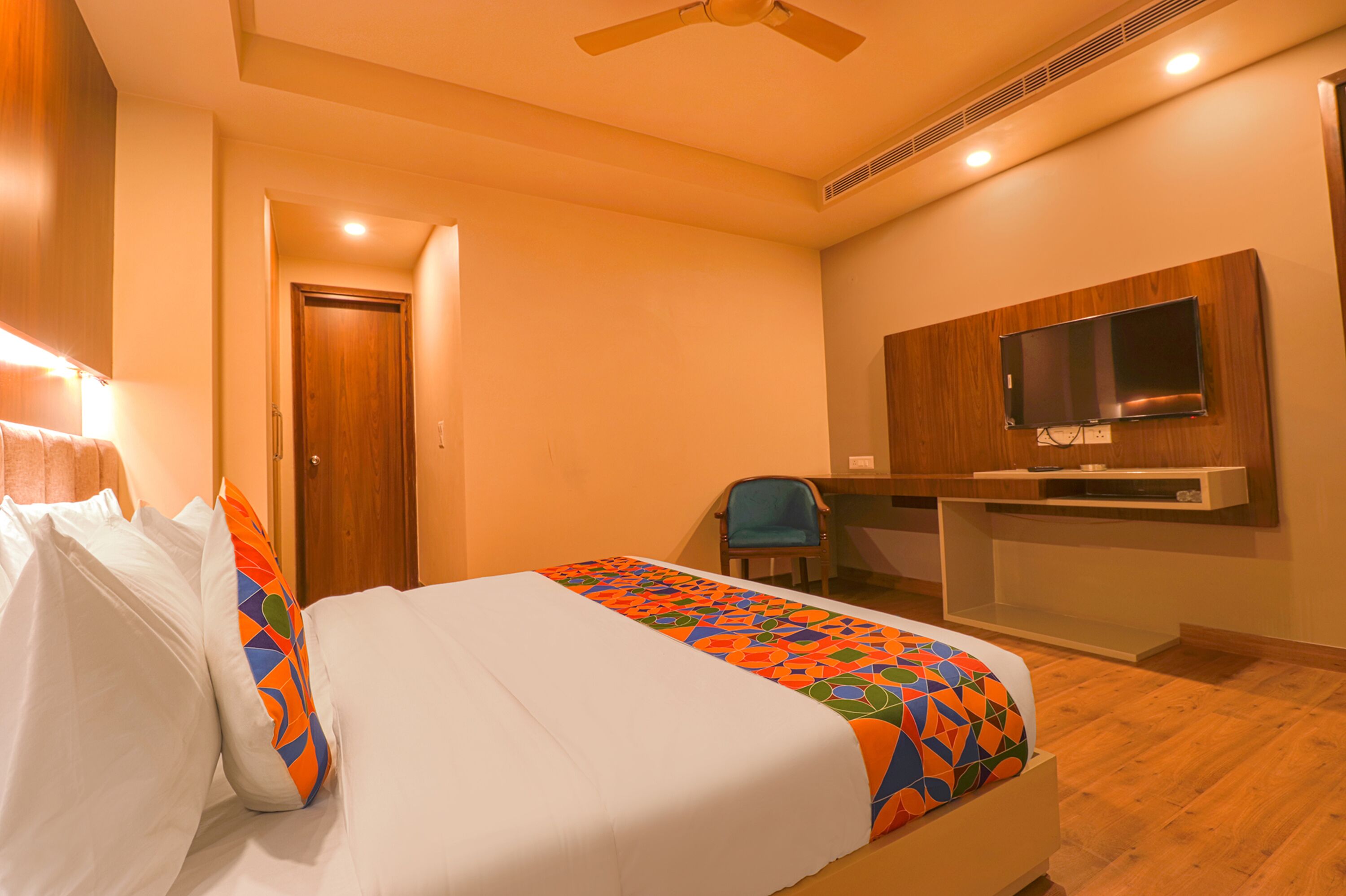 Una habitación de hotel con cama, escritorio, silla, televisor y puerta.
