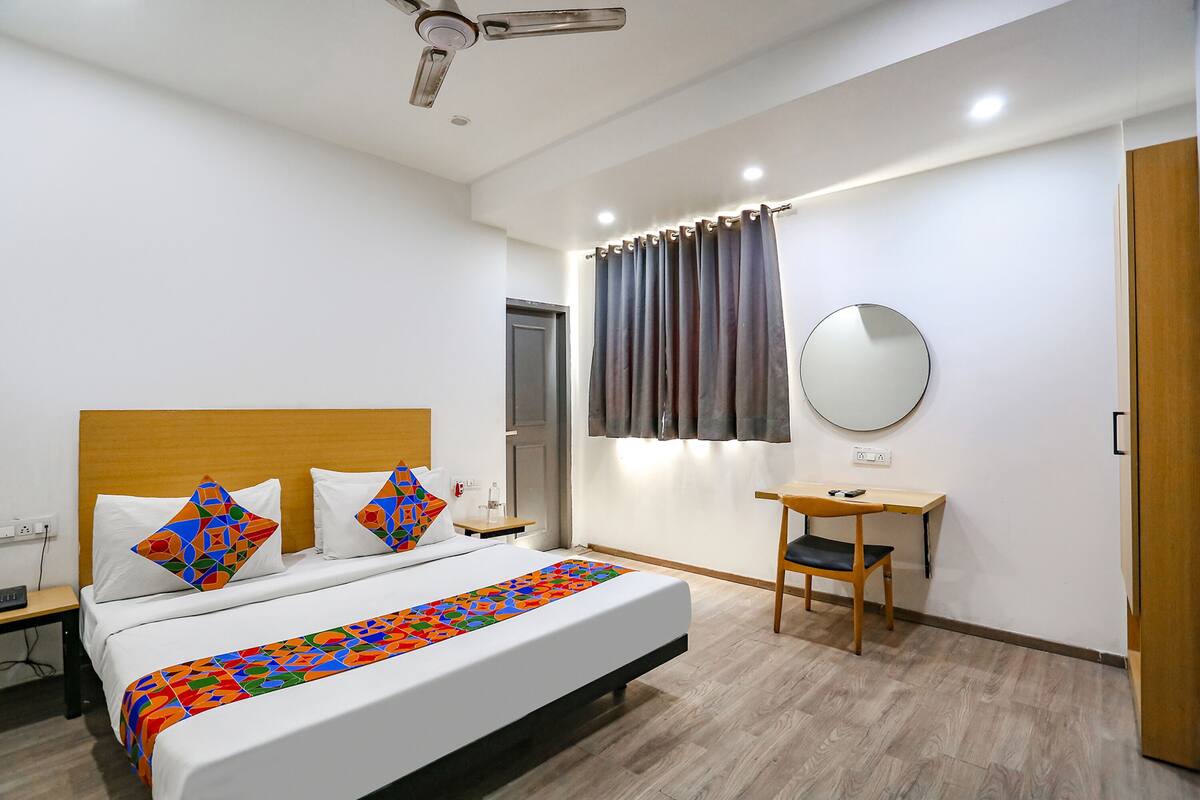A hotel room with a bed, a desk, a chair, a ceiling fan, a mirror, and a door.