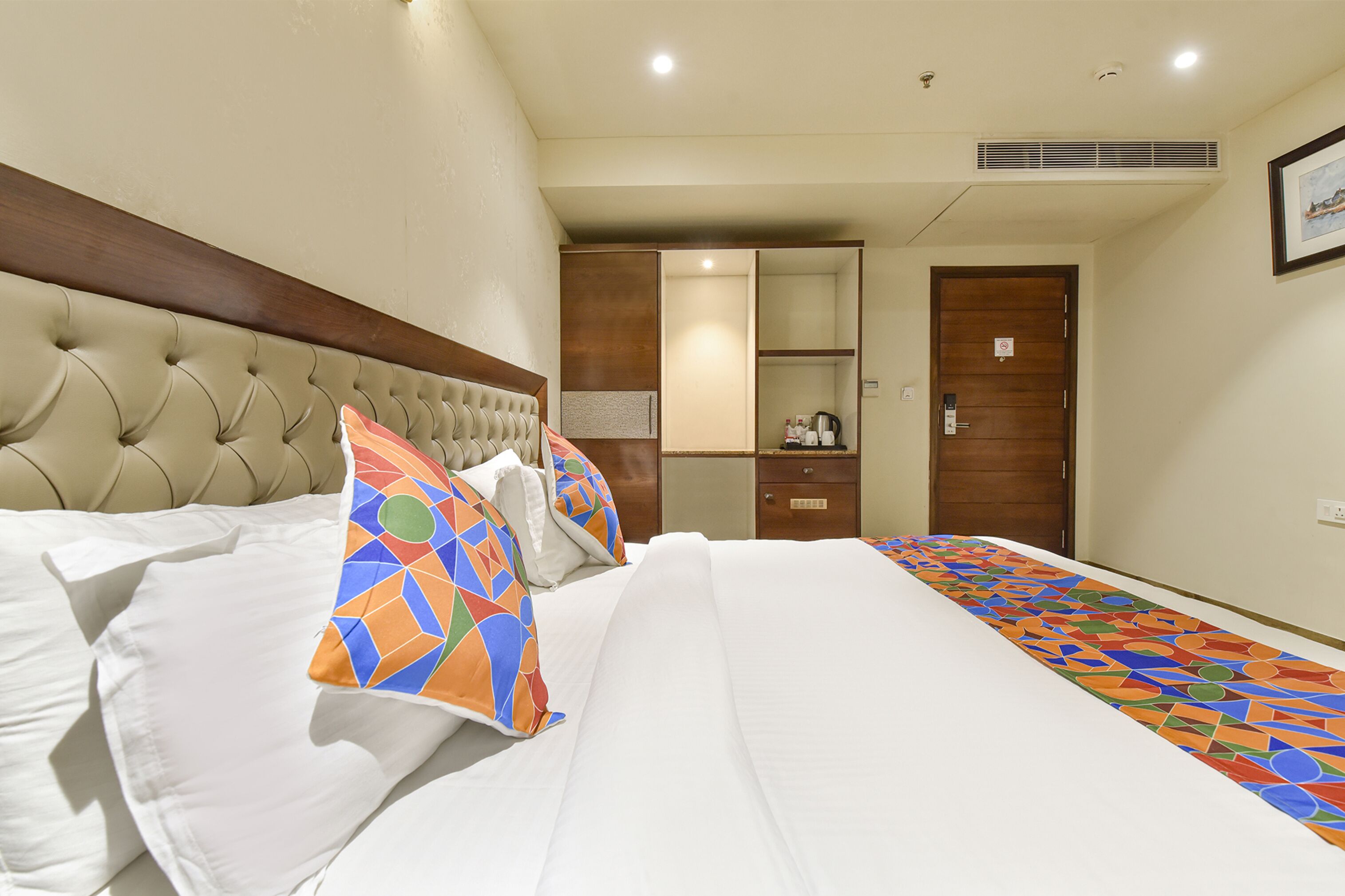 A hotel room with a large bed, a wooden headboard, a wardrobe, and a small desk with a chair.