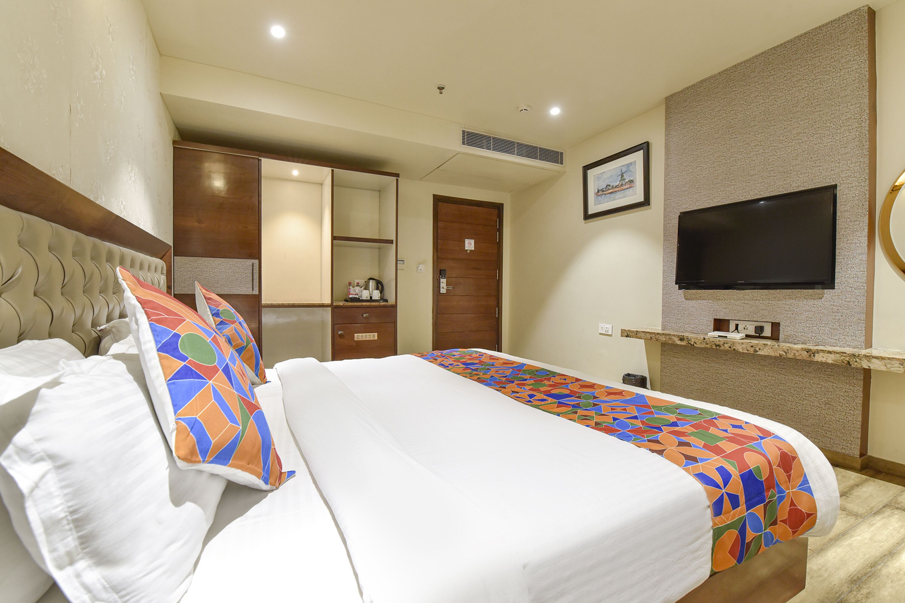 A hotel room with a bed, a TV, a wardrobe, and a desk with a chair.