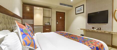 A hotel room with a bed, a TV, a wardrobe, and a desk with a chair.