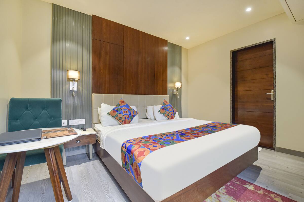 Habitación de hotel con una cama grande, un escritorio con silla, un armario de madera y una puerta.