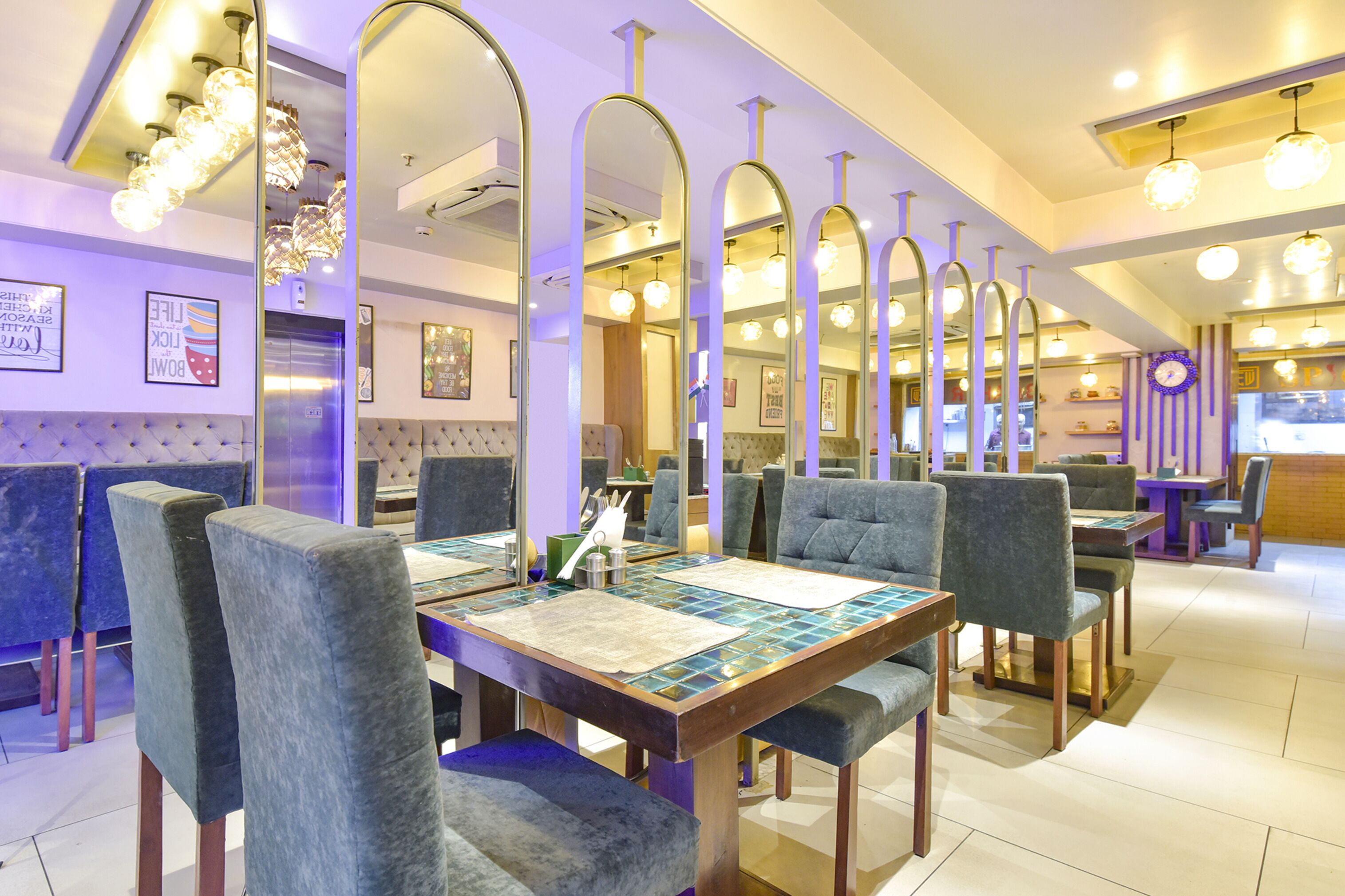 A restaurant with high-backed chairs, a long table with a decorative table runner, and multiple hanging light fixtures.