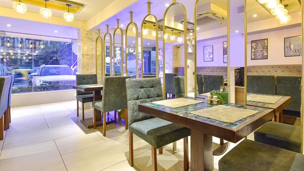 Un restaurant au décor moderne, avec un espace repas doté de chaises rembourrées et d’une table en bois, ainsi qu’une grande fenêtre offrant une vue sur la rue.