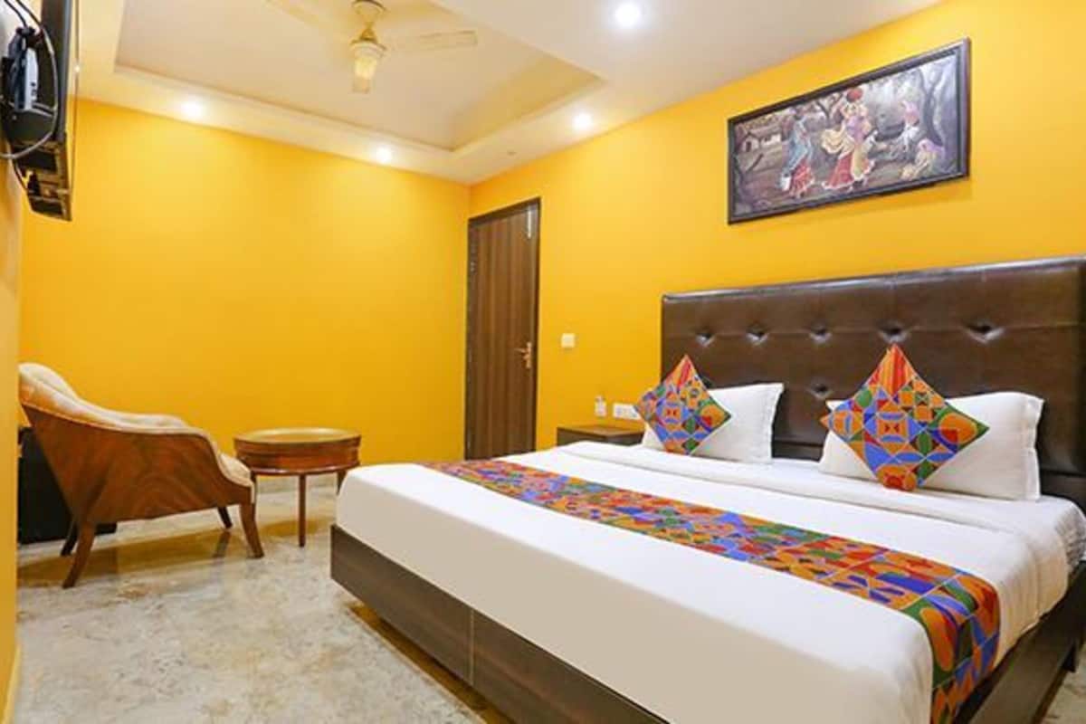 A hotel room with a large bed, a chair, a small table, and a painting on the wall.