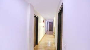 A long, narrow hallway with a polished wooden floor and white walls. There are doors on both sides, and a light fixture is visible on the wall. - FabHotel Taj Home Stay (New Delhi)