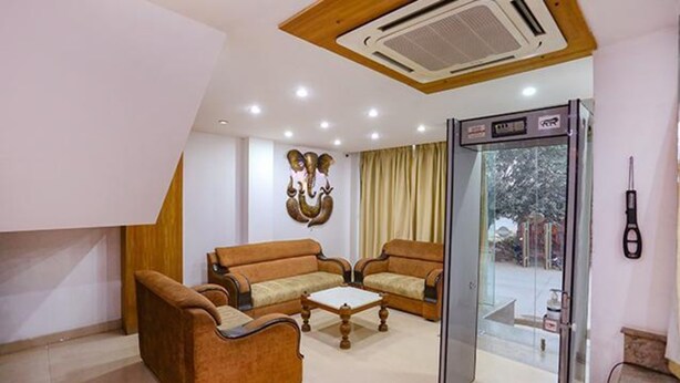 A hotel lobby with two sofas, a coffee table, a glass door leading outside, and a wall-mounted air conditioning unit. - FabHotel Taj Home Stay (New Delhi)