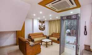 A hotel lobby with two sofas, a coffee table, a glass door leading outside, and a wall-mounted air conditioning unit. - FabHotel Taj Home Stay (New Delhi)