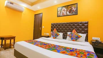 A hotel room with a large bed, a wooden nightstand, a brown upholstered headboard, and a painting on the wall.
