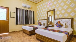 A hotel room with two beds, a wooden floor, a patterned wallpaper, an air conditioning unit, and a window with curtains. - Fabhotel Shivam Palace (Varanasi)