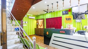 A hotel reception area with a staircase, reception desk, and a green wall with a 'fab hotels' sign. - Fabhotel Shivam Palace (Varanasi)