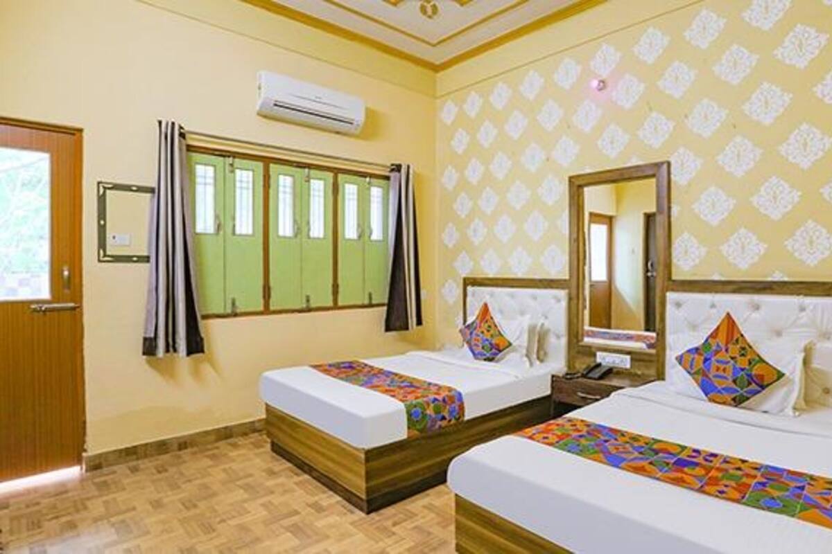 A hotel room with two beds, a window with curtains, an air conditioning unit, and a patterned wall.