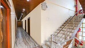 A hotel hallway with a marble floor, wooden doors, and a staircase with metal railings. - Fabhotel Shivam Palace (Varanasi)