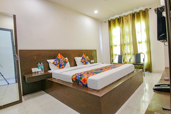 A hotel room with a large bed, a bedside table with water bottles, a TV, and a curtain. - Fabhotel Legacy (Chandigarh)