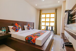 A hotel room with a large bed, a desk, a chair, and a window with curtains. - Fabhotel Legacy (Chandigarh)