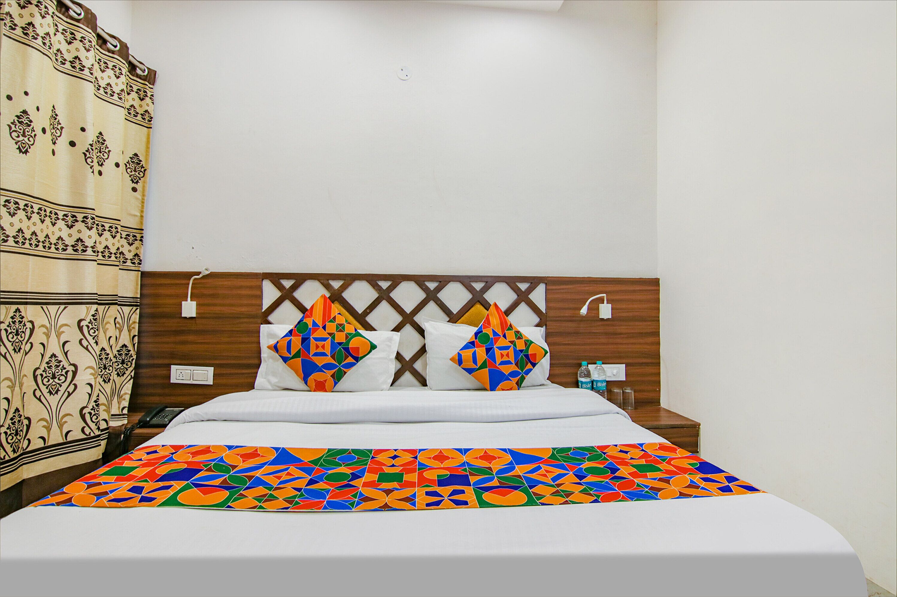 A neatly made bed with a colorful geometric-patterned bedspread, a wooden headboard with a lattice design, and a bedside table with a water bottle and a phone.