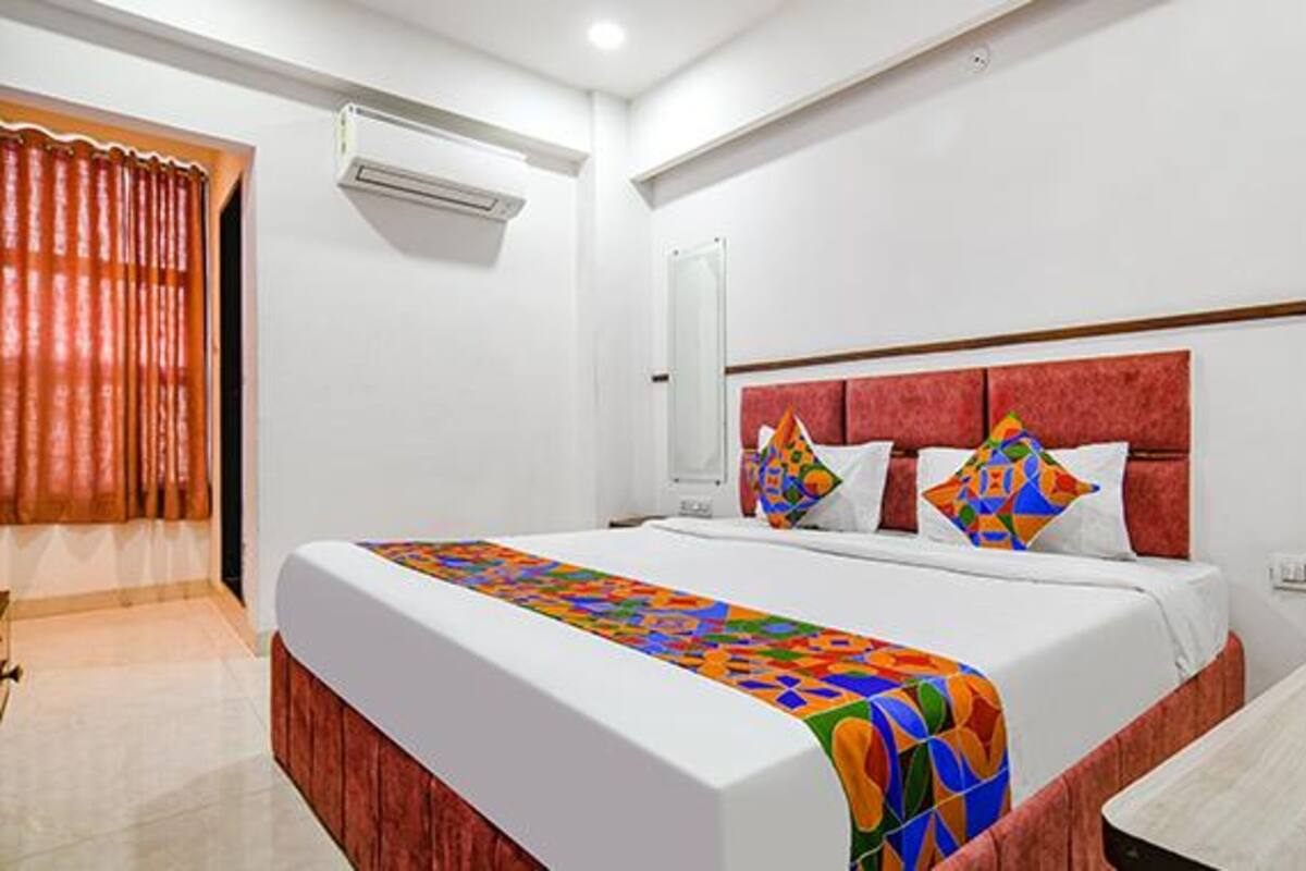 A hotel room with a large bed, a bedside table, a mirror, and an air conditioning unit.