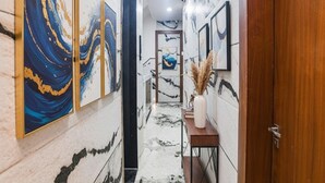 A hallway with marble walls and floor, featuring framed artwork and a wooden door. - Fabhotel Elite Residency (Indore)