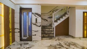 A modern interior with a marble floor, a glass door entrance, and a staircase with a glass railing. - Fabhotel Elite Residency (Indore)