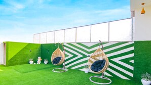 Un jardín en la azotea con césped artificial, tres sillas colgantes y plantas en macetas.