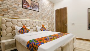 Una habitación de hotel con una pared de ladrillo, una puerta de madera, una cama con colcha de estampado geométrico y una mesita de noche con cajón.