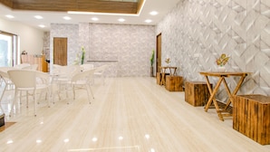 Un lobby moderno de hotel con mostrador de recepción, sillas blancas, una mesa de centro de madera y una pared decorativa.