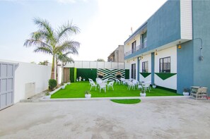 A courtyard with white chairs and tables, a green lawn, and a building with a blue exterior. - FabHotel Sky Lark Farm (Ludhiana)
