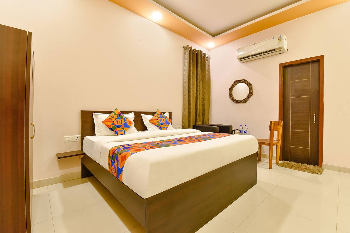 A neatly arranged hotel room with a large bed, a wooden headboard, a small desk, a chair, and a wardrobe.