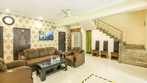A living room with a sofa, armchairs, a coffee table, and a staircase. - FabExpress Alacia Inn (Lucknow)