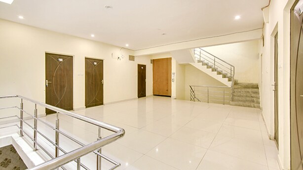 A spacious, well-lit hallway with a polished floor, a metal railing, and a staircase leading to another level. - FabExpress Alacia Inn (Lucknow)