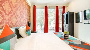 A hotel room with a large bed, red curtains, a TV, and a wardrobe. - FabExpress Alacia Inn (Lucknow)