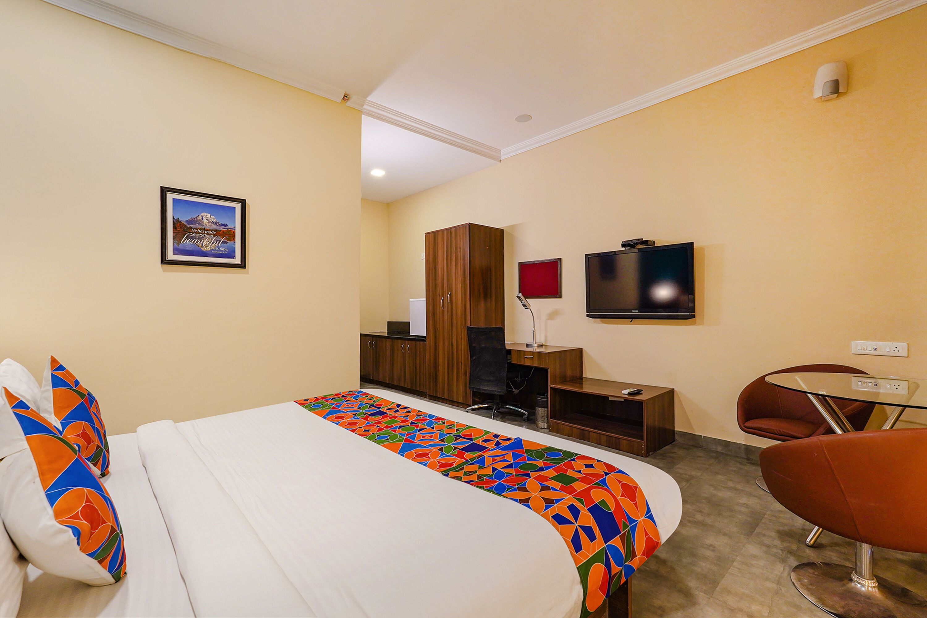 A hotel room with a bed, a desk with a chair, a television, and a small table with a chair.