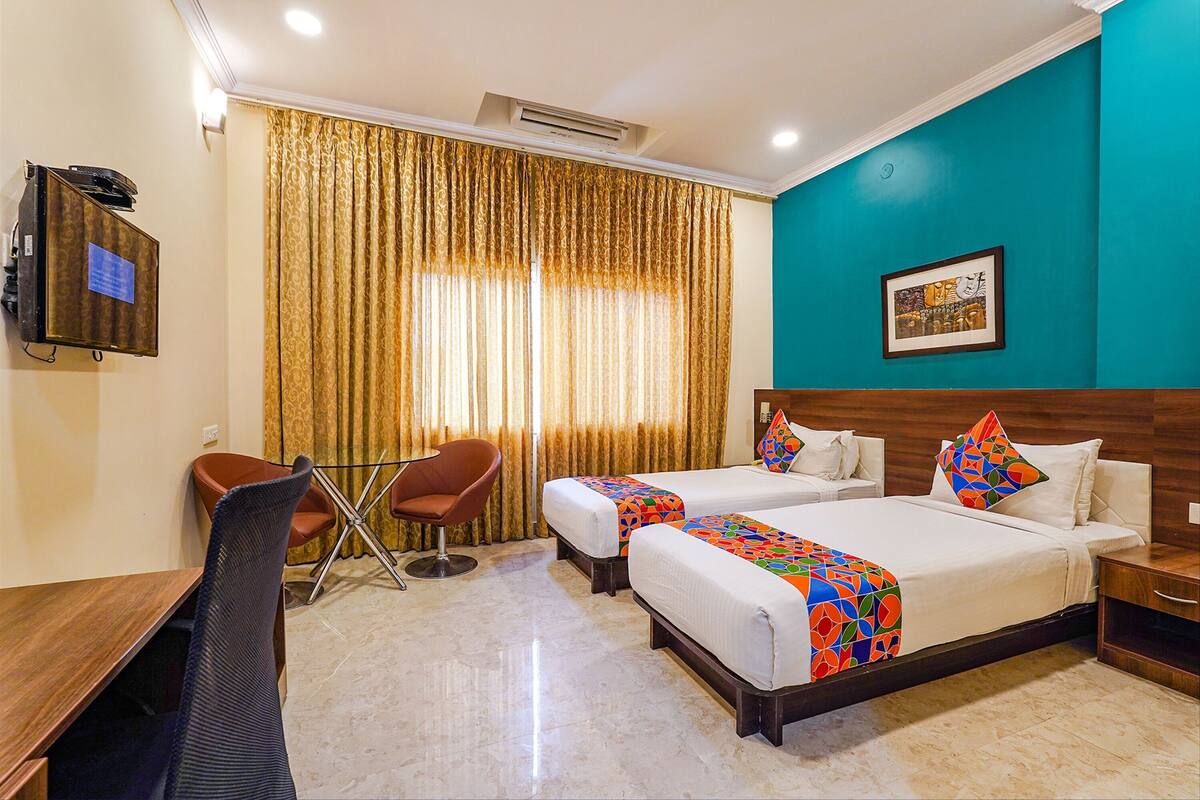 A hotel room with two beds, a desk, a chair, and a TV.