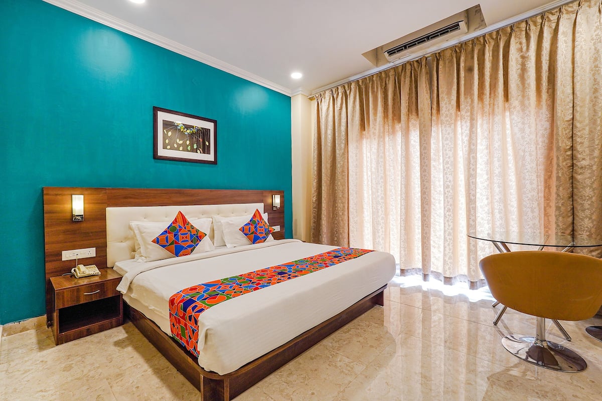 A hotel room with a large bed, a nightstand, a chair, and a window with curtains.