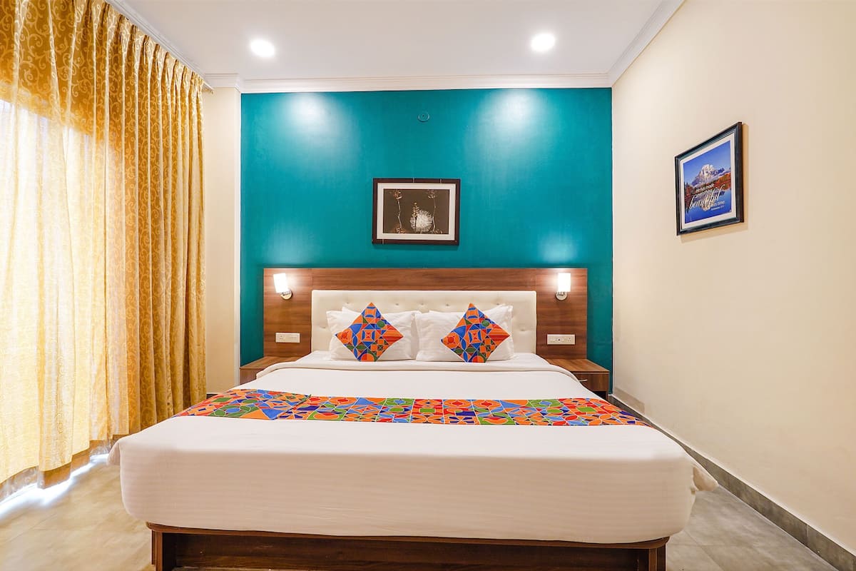 A hotel room with a bed, a headboard, a wall-mounted picture, and a window with curtains.