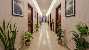 A long, well-lit hallway with wooden doors, potted plants, and framed artwork on the walls. - FabHotel Chris - Whitefield near KTPO & ITPL (Bengaluru)