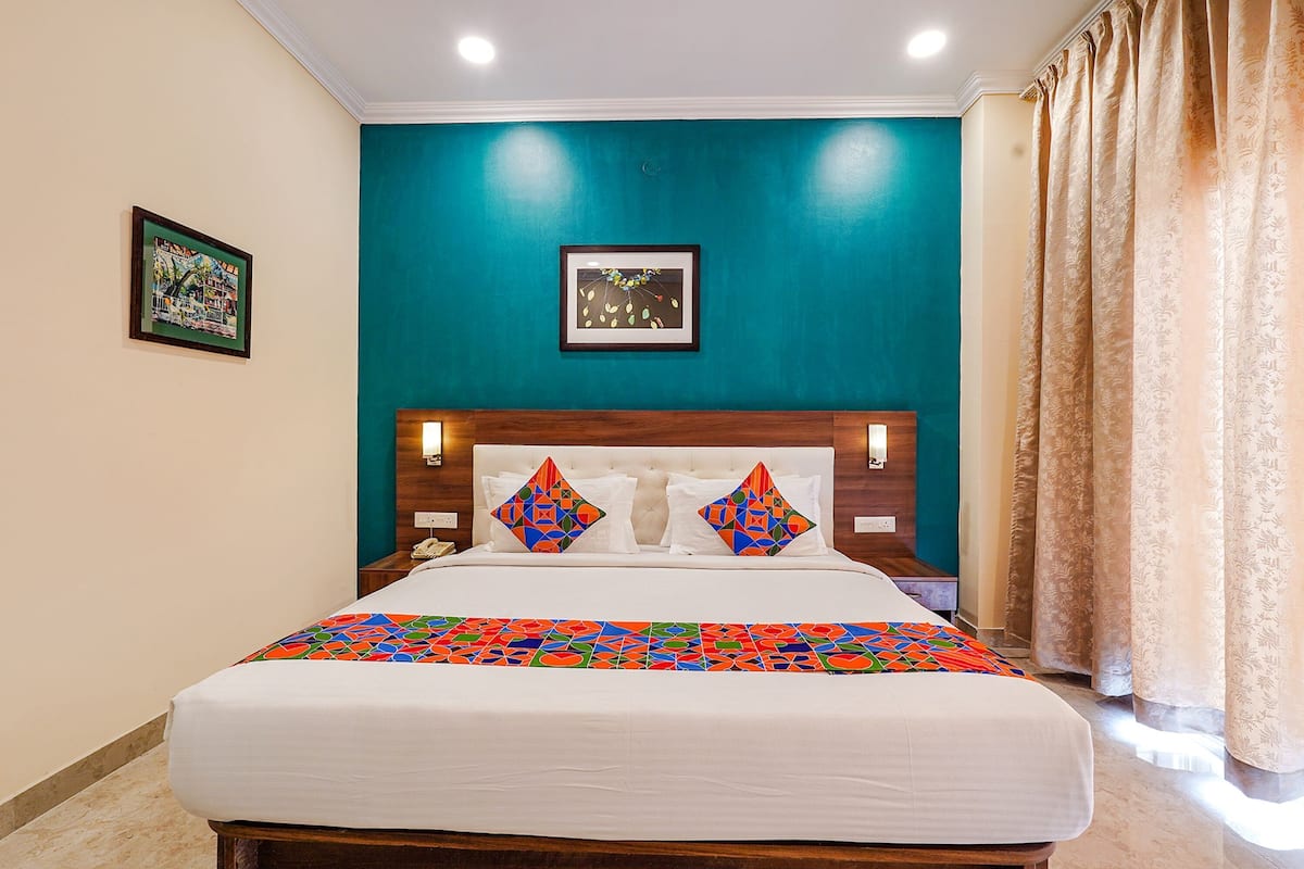 A hotel room with a bed, teal walls, and a window with curtains.