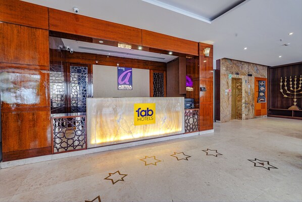 Zona de recepción de hotel con fachada de madera, un letrero de 'fab hotels' y un letrero de 'Astra Hotel & Suites'.