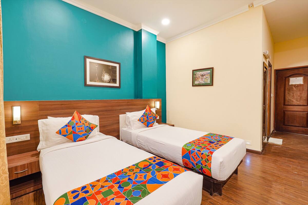 A hotel room with two single beds, teal walls, wooden headboards, and a wooden floor.