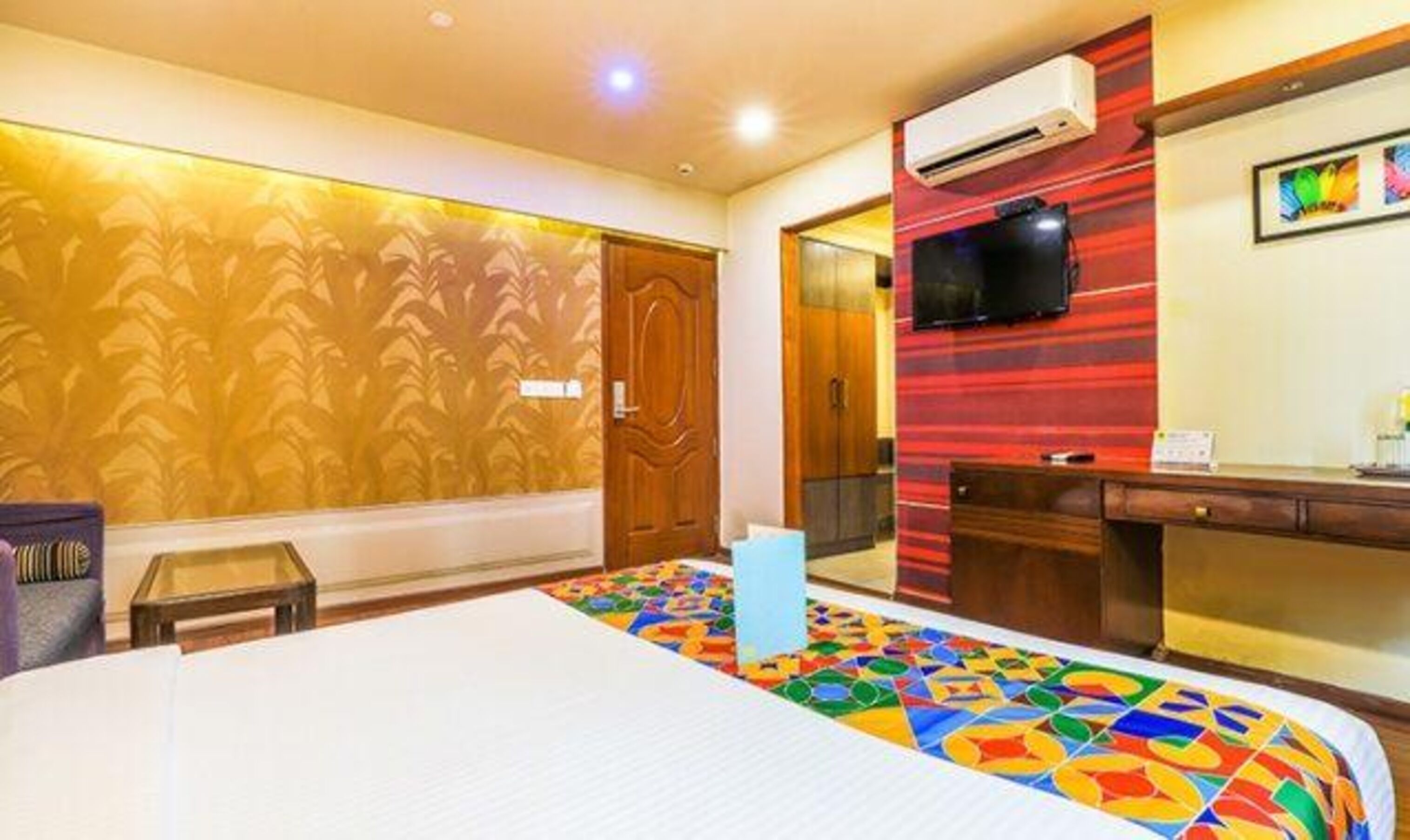 A hotel room with a large bed, a desk, an air conditioning unit, and a television on the wall.