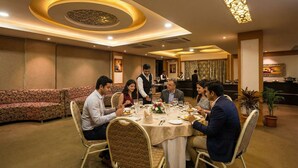 A formal dining room with a round table, guests seated, and waitstaff attending to them. - Fabhotel Astra Berry'S (Bengaluru)