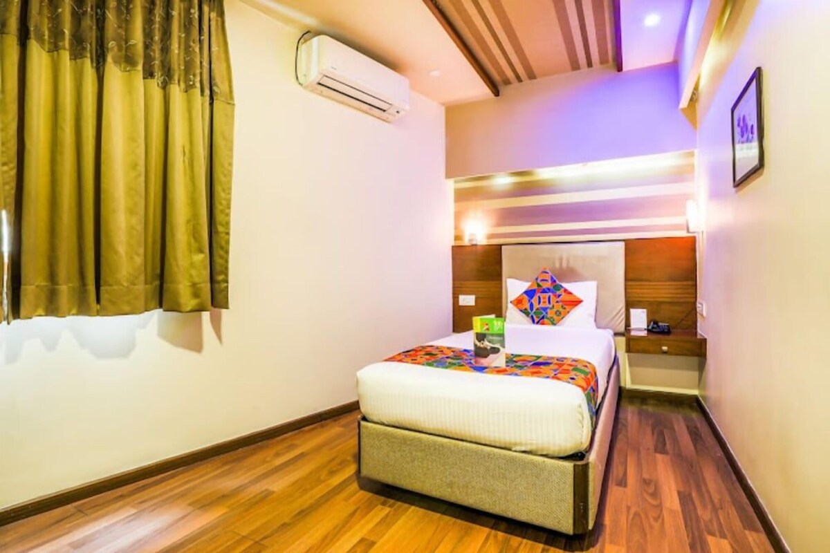 A hotel room with a bed, bedside table, and an air conditioning unit.